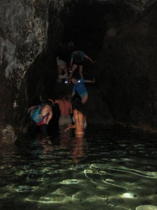 Climbing over a boulder into the cold water in the dark lava tunnel